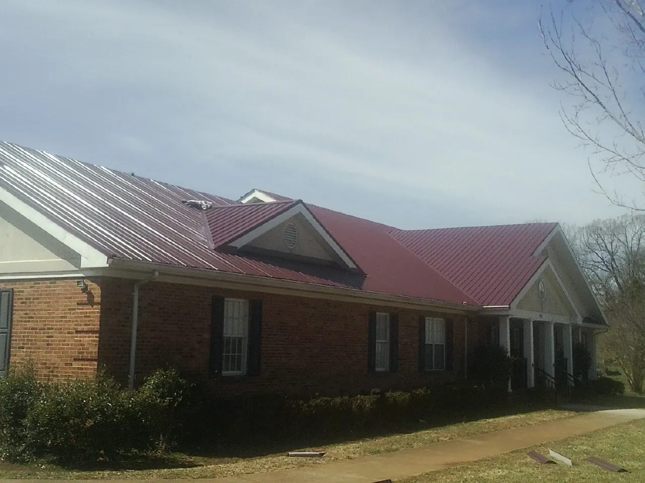 Red metal roof with gabled entries on a long brick building, from a Hail Damage Roof Repair job in Pecatonica