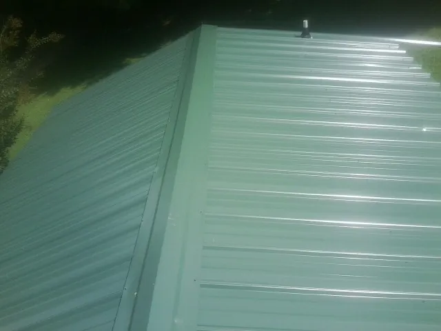 New green metal panels meeting at the ridge of a roof — Flat Roof Repair work by our crew in Pecatonica