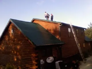 Crew on the ridge of a green metal roof on a two story log home in Pecatonica