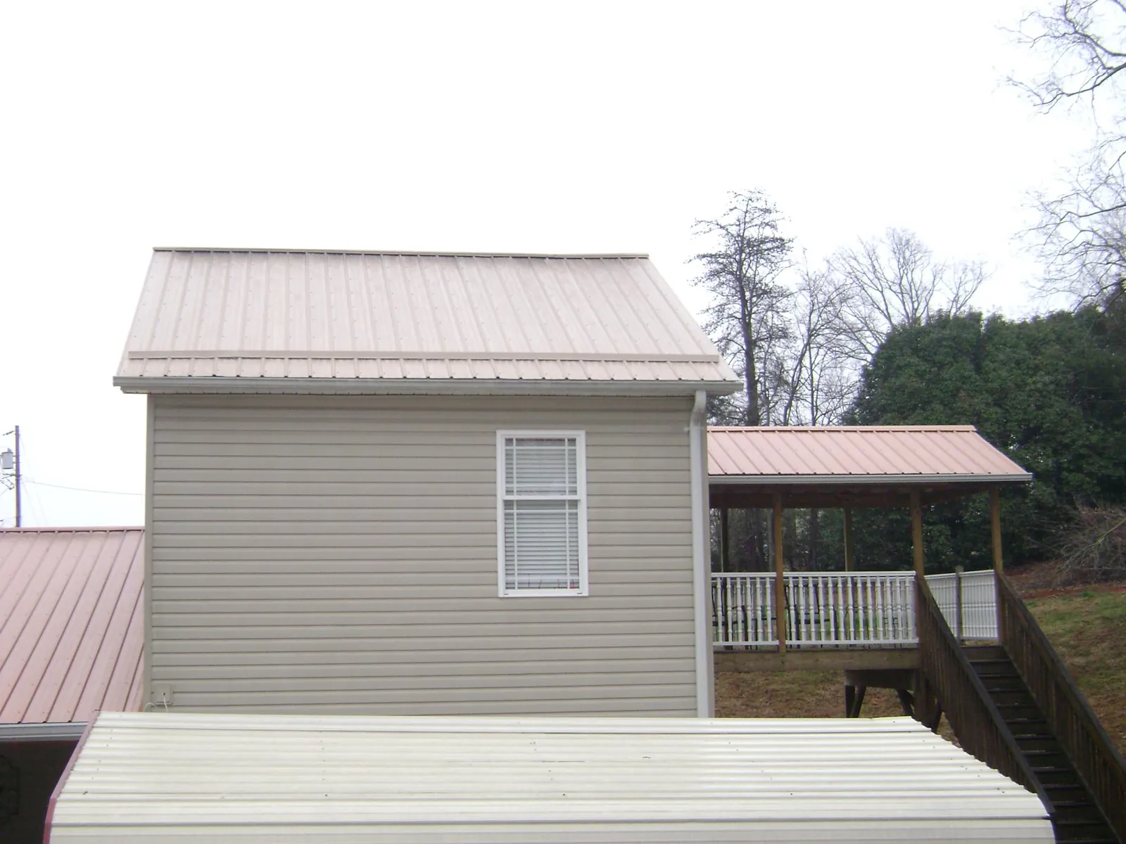 Tan metal roofs on a two story addition and attached porch, from a Roof Replacement job in Pecatonica